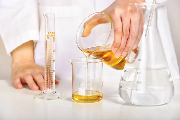 Un'operatrice versa un olio cosmetico dorato in un becher graduato